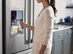 Person using a refrigerator's water dispenser with a glass containing lemon slices.